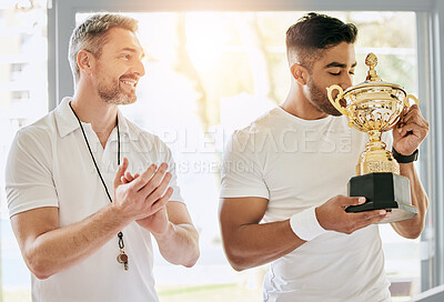 Buy stock photo Cropped shot of a handsome young male tennis player kissing a trophy while his coach watches on and applauds