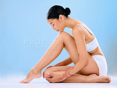 Buy stock photo Studio shot of a beautiful young woman sitting in her underwear and posing against a blue background