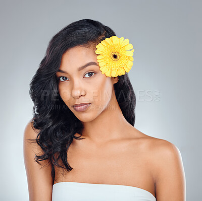 Buy stock photo Studio portrait of an attractive young woman posing with a yellow flower in her hair against a grey background
