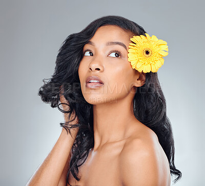 Buy stock photo Studio shot of an attractive young woman posing with a yellow flower in her hair against a grey background