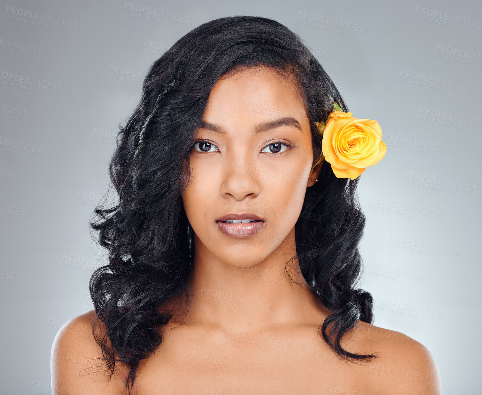 Buy stock photo Studio portrait of an attractive young woman posing with a yellow flower in her hair against a grey background