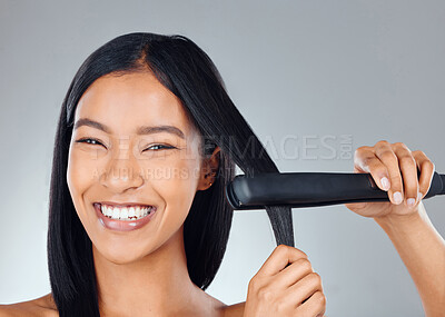 Buy stock photo Studio portrait of an attractive young woman using a flat iron to straighten her hair against a grey background