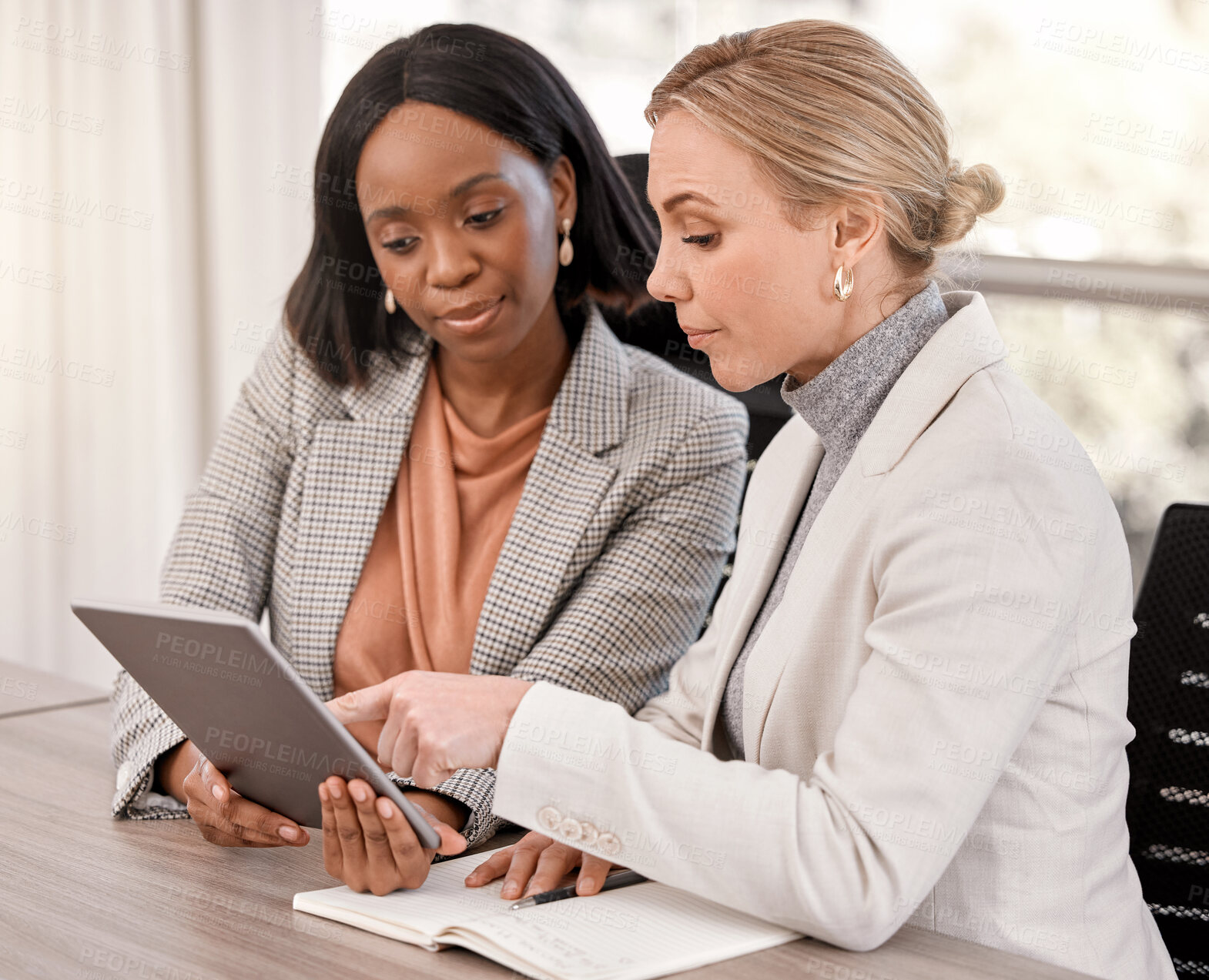 Buy stock photo Shot of two businesswomen planning together while using a digital tablet