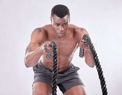 Buy stock photo Studio shot of a muscular young man exercising with battle ropes against a grey background