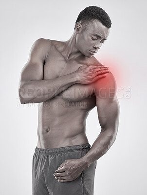 Buy stock photo Black and white shot of a muscular young man experiencing shoulder pain against a grey background