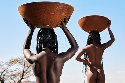 Buy stock photo Rearview shot of two unrecognizable young women carrying pots on their heads outside