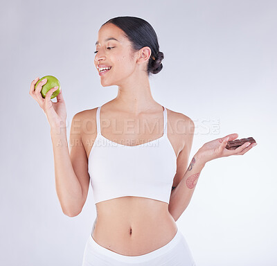 Buy stock photo Studio shot of a young woman deciding between and apple and a chocolate against a white background