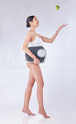 Buy stock photo Studio shot of a young woman tossing an apple while holding a scale against a white background