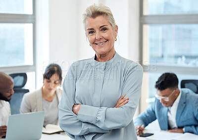 Buy stock photo Portrait of a mature businesswoman standing with her arms crossed in an office with her colleagues in the background