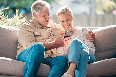 Buy stock photo Smile, senior couple and sofa with phone for browsing social media, streaming video and reading online news. Happy elderly woman and man with mobile of communication, article or hug together at house