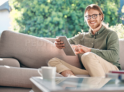 Buy stock photo Portrait of a young man using a digital tablet while relaxing on the sofa at home