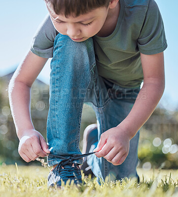 Buy stock photo Shot of an adorable little boy tying his shoelaces outside