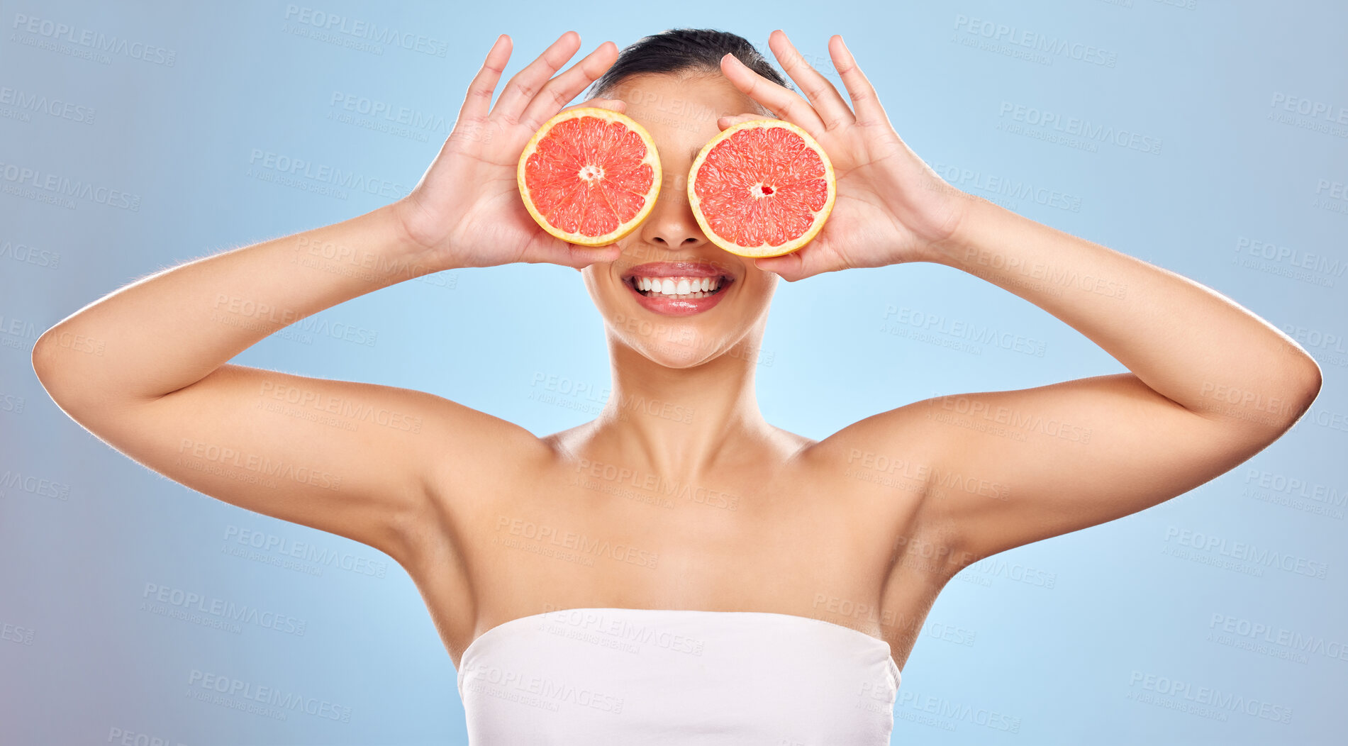 Buy stock photo Girl, grapefruit and eyes in studio for skincare, organic and natural cosmetics with vitamin c or citrus. Woman, hands and fruit on blue background for hyperpigmentation, detox and healthy glow.