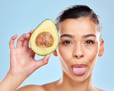 Buy stock photo Studio portrait of an attractive young woman sticking out her tongue while posing with an avocado against a blue background