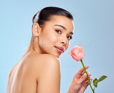 Buy stock photo Studio portrait of an attractive young woman posing with a pink rose against a blue background