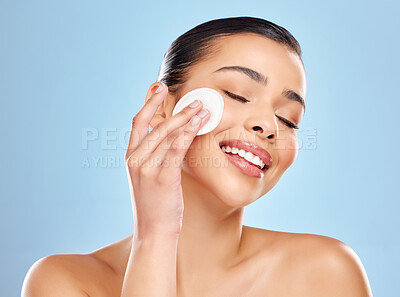 Buy stock photo Studio shot of an attractive young woman using a cotton pad on her face against a blue background
