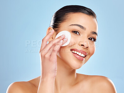 Buy stock photo Studio portrait of an attractive young woman using a cotton pad on her face against a blue background