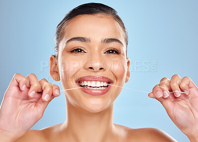 Buy stock photo Studio portrait of an attractive young woman flossing her teeth against a blue background