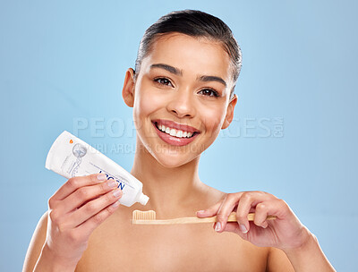 Buy stock photo Studio portrait of an attractive young woman applying toothpaste to a toothbrush against a blue background
