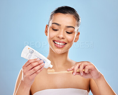 Buy stock photo Studio shot of an attractive young woman applying toothpaste to a toothbrush against a blue background
