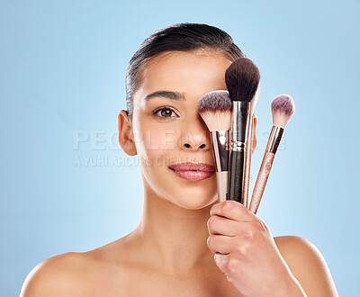 Buy stock photo Studio portrait of an attractive young woman holding a collection of makeup brushes against a blue background