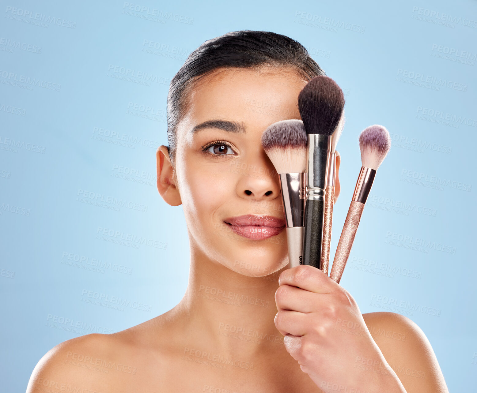 Buy stock photo Studio portrait of an attractive young woman holding a collection of makeup brushes against a blue background
