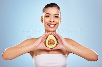 Buy stock photo Studio portrait of an attractive young woman posing with an avocado against a blue background