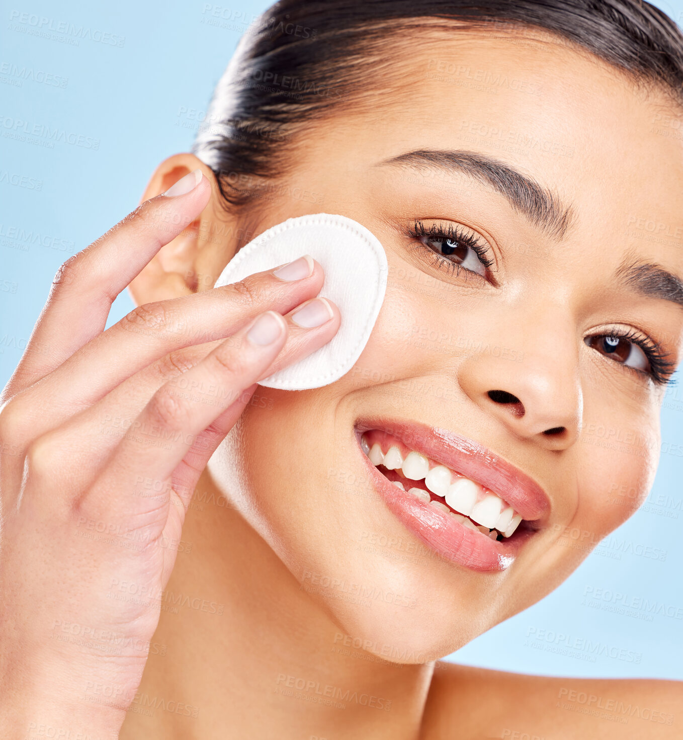 Buy stock photo Studio portrait of an attractive young woman using a cotton pad on her face against a blue background