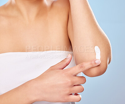 Buy stock photo Studio shot of an unrecognisable woman applying lotion to her elbow against a blue background