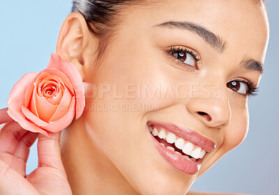 Buy stock photo Studio portrait of an attractive young woman posing with a pink rose against a blue background