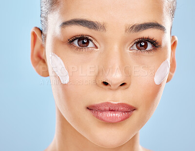 Buy stock photo Studio portrait of an attractive young woman posing with moisturiser on her face against a blue background