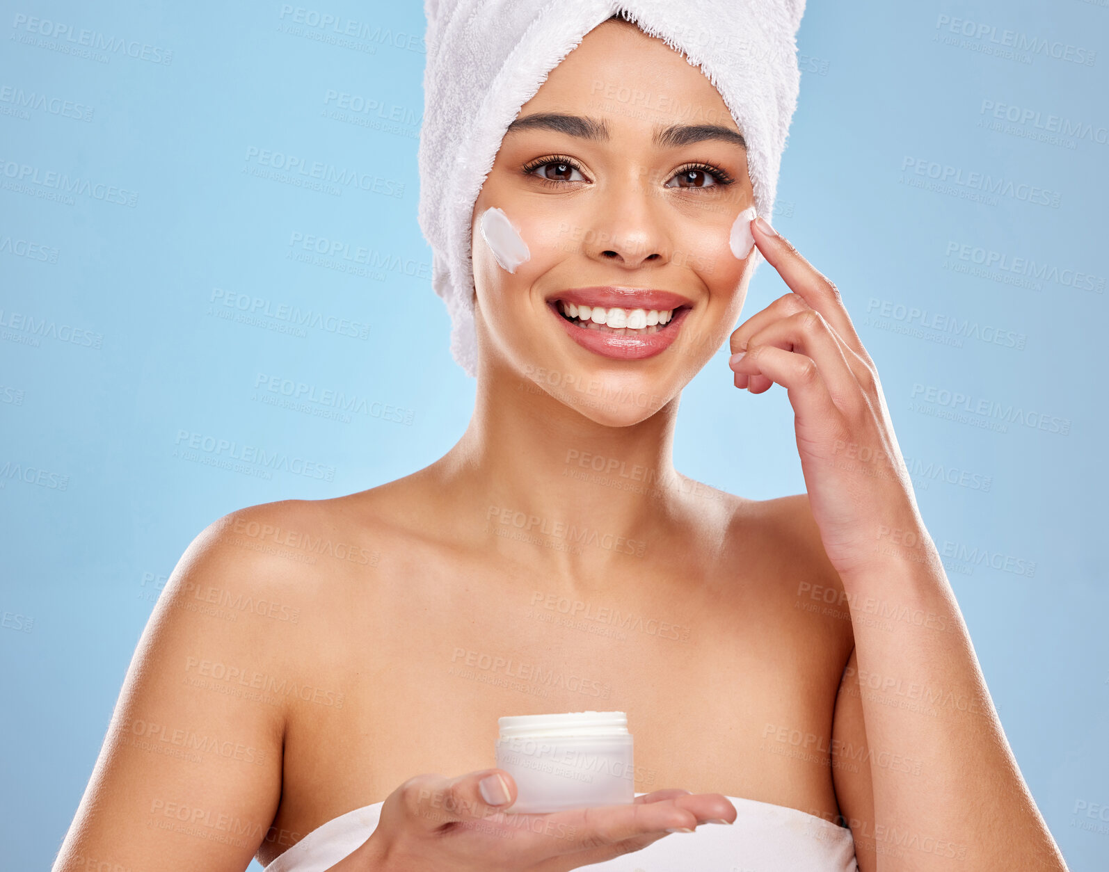 Buy stock photo Apply cream, hands and woman portrait in studio for skincare treatment, cosmetics or dermatology spa on blue background. Beauty, towel and happy model with product for shine, moisturizer or wellness