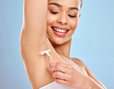 Buy stock photo Studio shot of an attractive young woman shaving her underarm against a blue background
