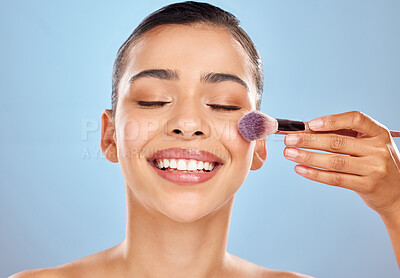 Buy stock photo Studio shot of an attractive young woman applying makeup to her face with a brush against a blue background