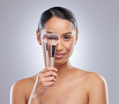 Buy stock photo Shot of an attractive young woman standing alone in the studio and holding makeup brushes