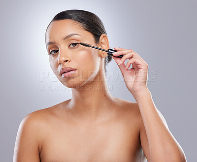 Buy stock photo Shot of an attractive young woman standing alone in the studio and applying mascara