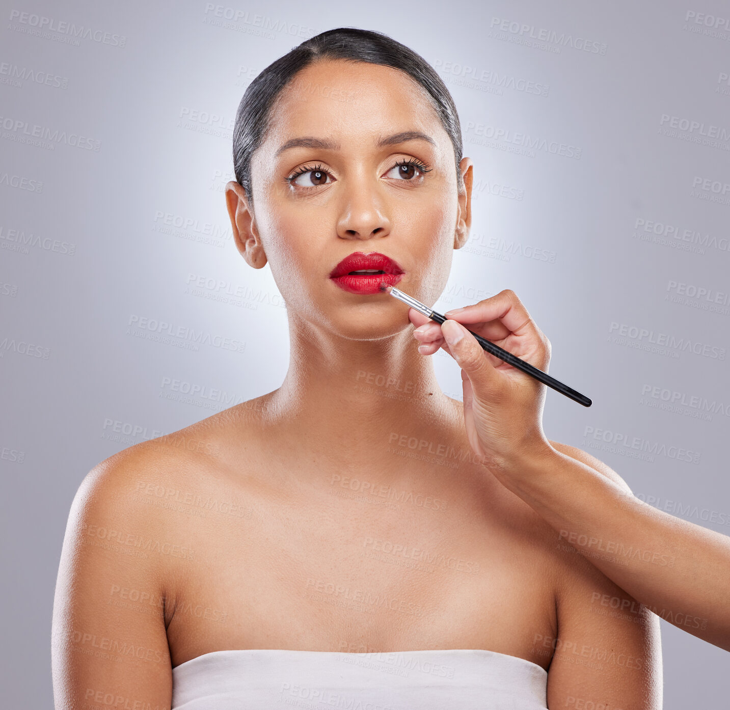 Buy stock photo Shot of an attractive young woman standing in the studio while a makeup artist applies lipstick