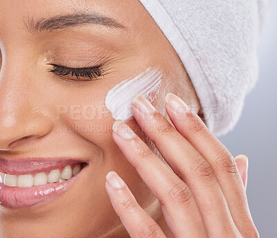 Buy stock photo Cropped shot of an attractive young woman applying moisturiser to her skin in the studio
