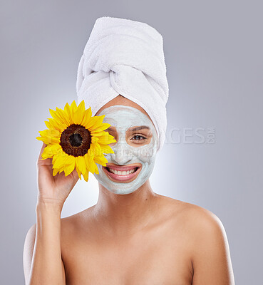 Buy stock photo Shot of an attractive young woman wearing a face mask and holding a sunflower over her eye in the studio