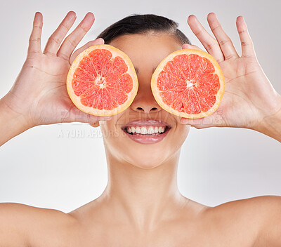 Buy stock photo Studio portrait of a young woman posing with half a grapefruit against a grey background