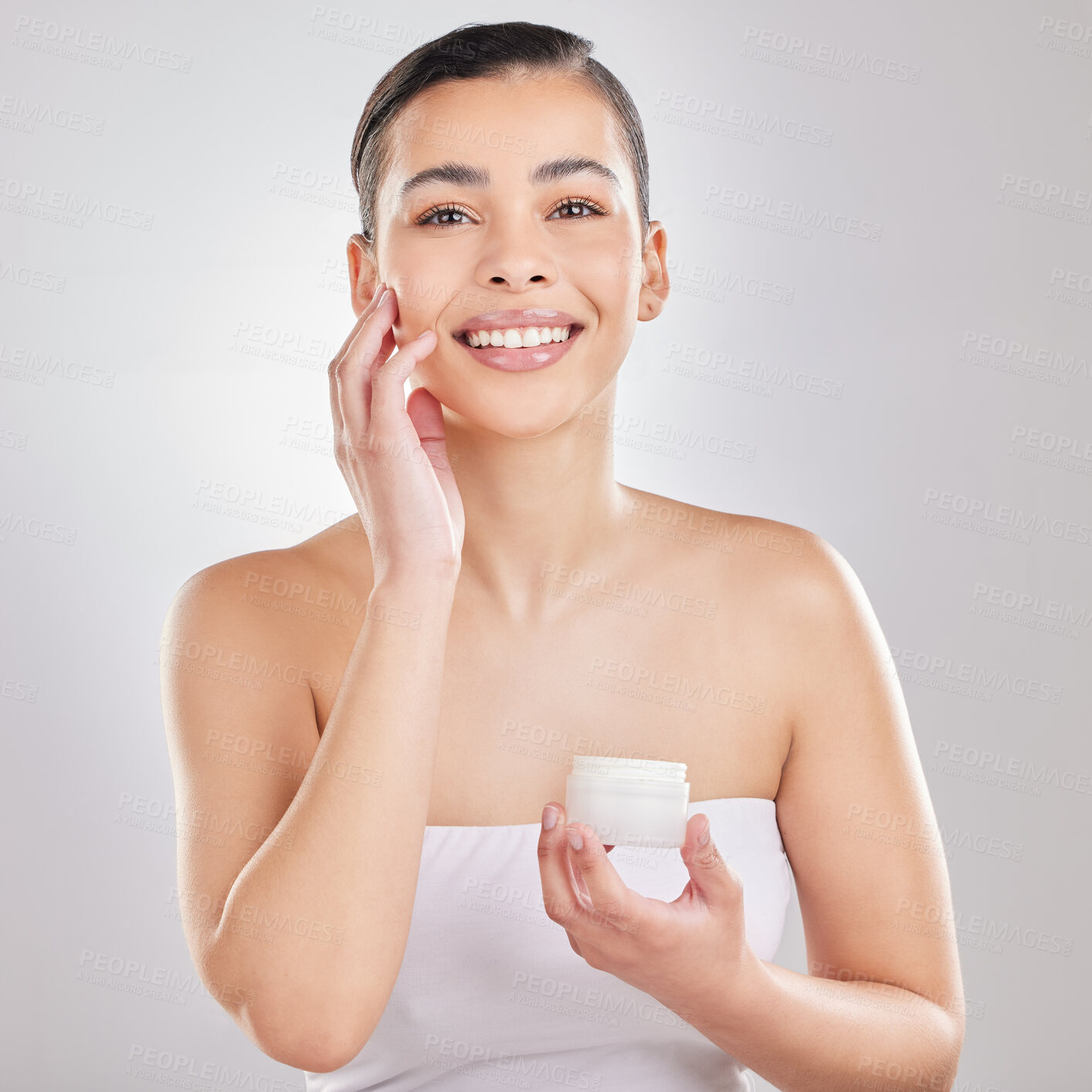 Buy stock photo Shot of a young woman applying a cream to her face against a grey background