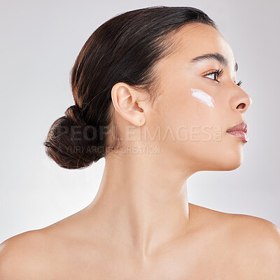 Buy stock photo Shot of a young woman applying a cream to her face against a grey background