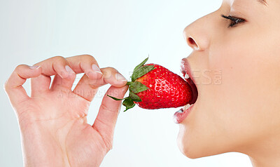 Buy stock photo Studio shot of an attractive young woman biting into a strawberry against a light background