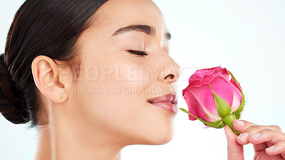 Buy stock photo Studio portrait of an attractive young woman smelling a pink rose against a light background