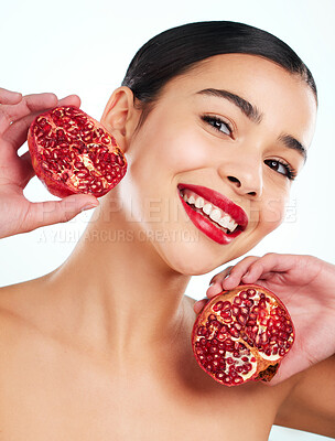 Buy stock photo Studio portrait of an attractive young woman posing with a pomegranate against a light background