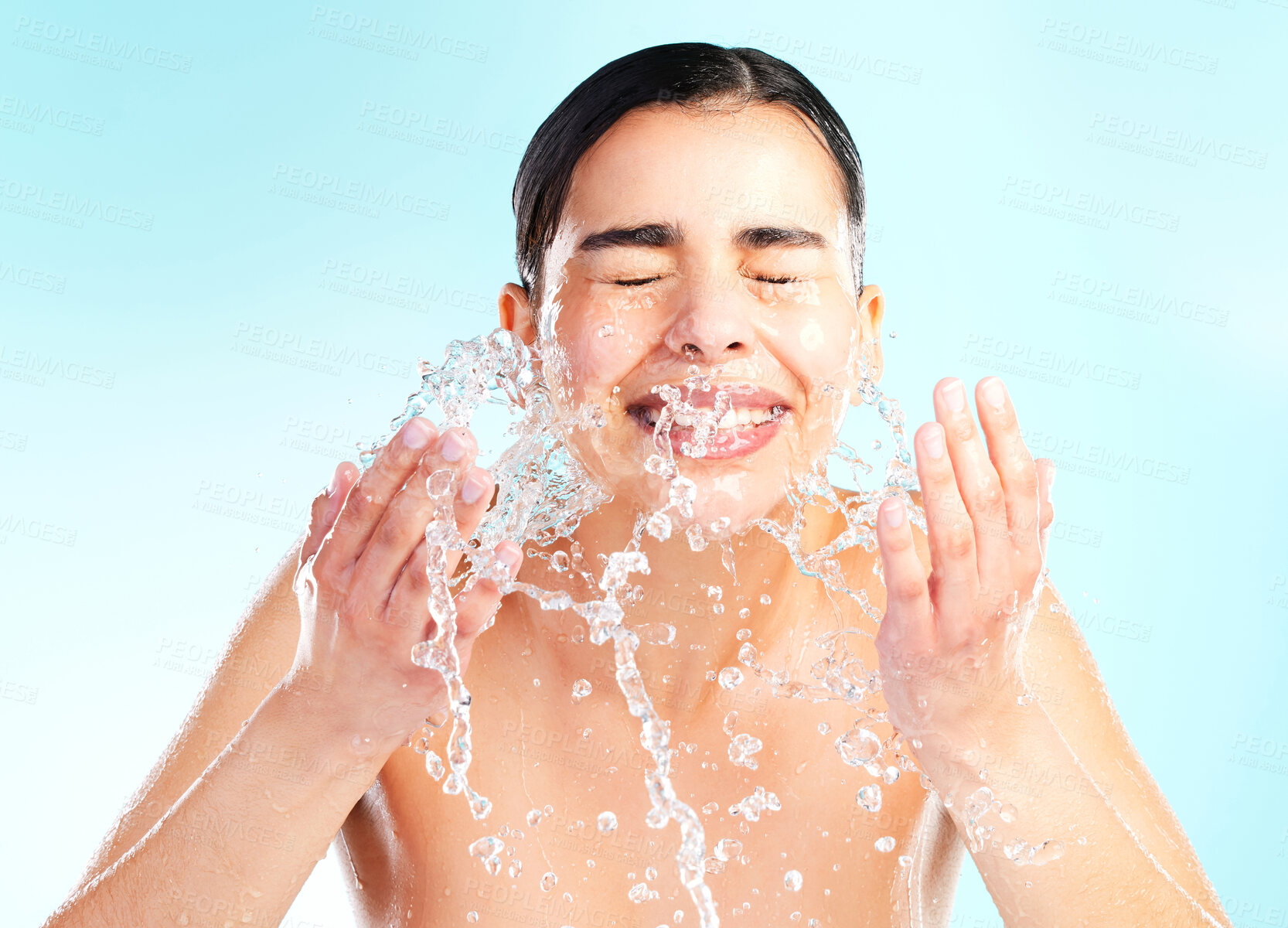 Buy stock photo Wellness, woman and splash or water in studio for skincare, dermatology and glow or smile. Hygiene, model girl and happy or hands with liquid for facial and aesthetic or shine by blue background 