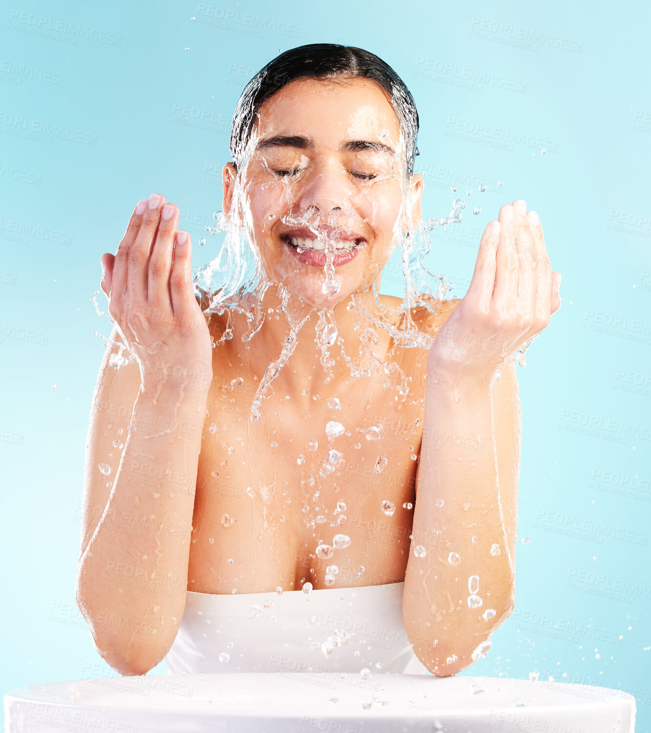 Buy stock photo Skincare, woman and beauty or water in studio for cleaning, dermatology and glow or wellness. Hygiene, model girl and hands or smile and splash for facial and aesthetic or shine by blue background 