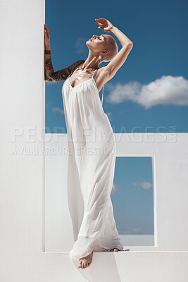 Buy stock photo Shot of an attractive young woman posing on top of a white wall against a sunny sky