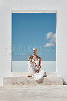 Buy stock photo Shot of an attractive young woman posing on top of a white wall against a sunny sky