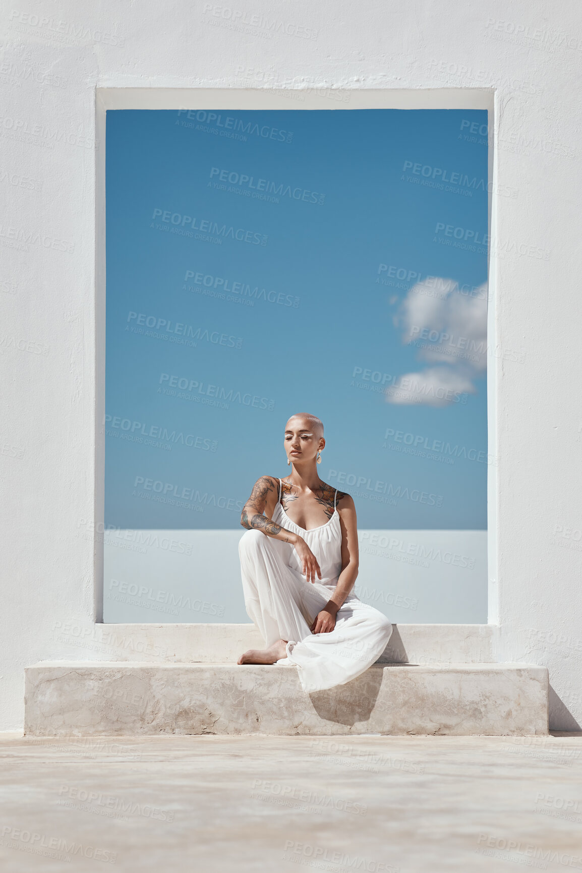 Buy stock photo Shot of an attractive young woman posing on top of a white wall against a sunny sky